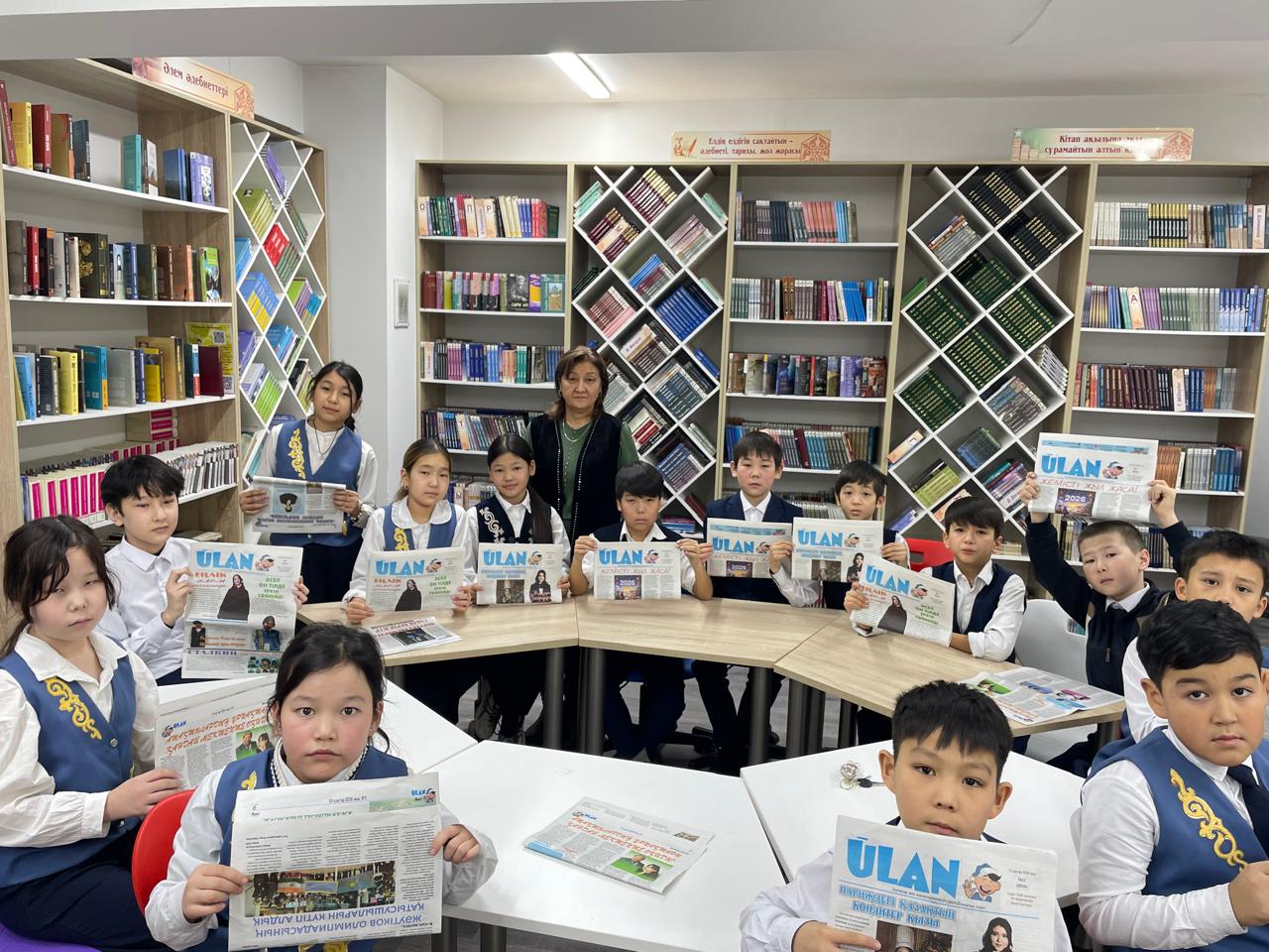 Кітапханада 5 Е сынып оқушылары Ұлан газетімен танысу үстінде Сынып жетекшісі Досжанова Н және кітапханашы Садыбаева Ф
